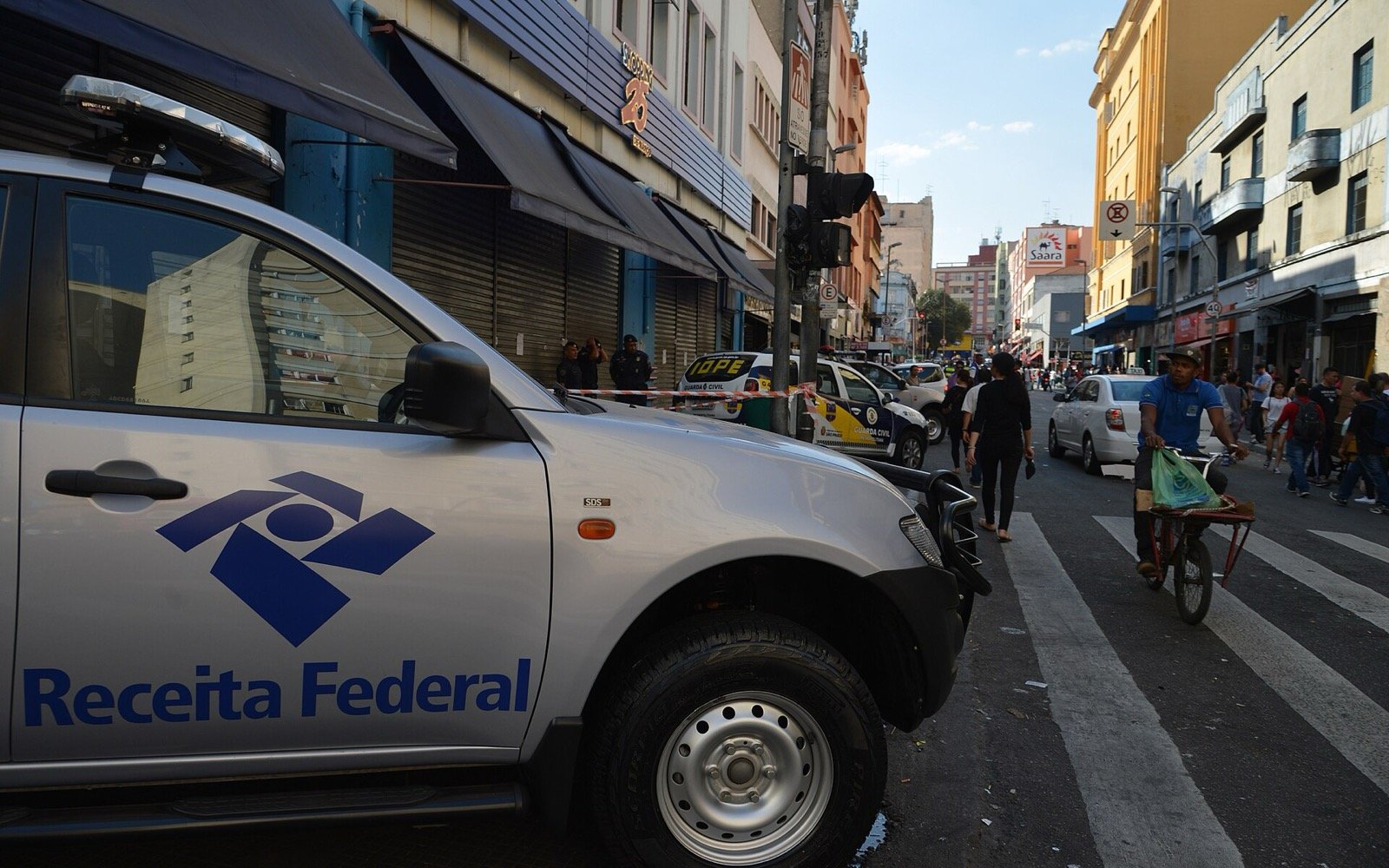 Viatura da Receita Federal estacionada em rua de comércio popular, com lojas e pedestres ao fundo