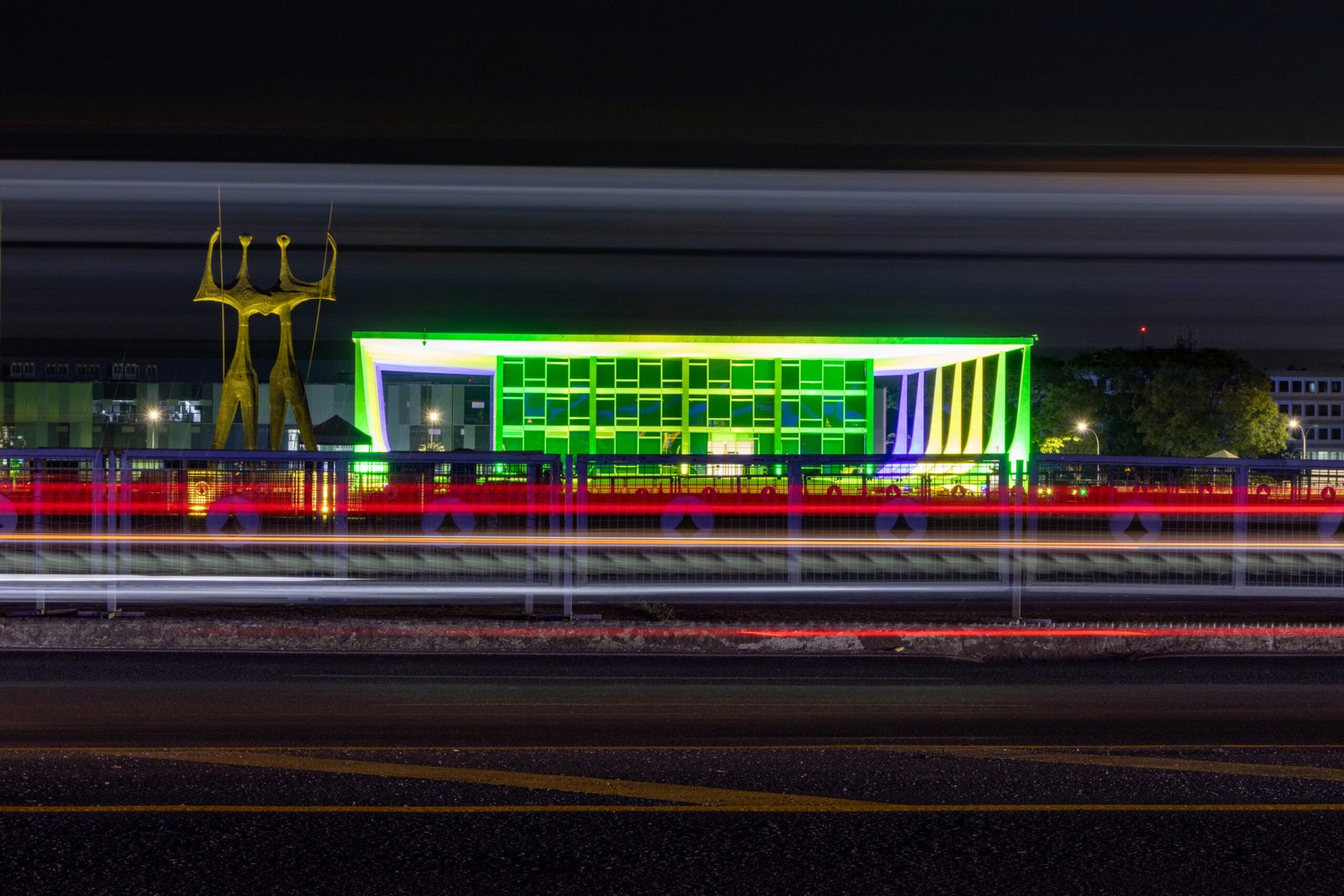 Edifício do Supremo Tribunal Federal iluminado em verde e amarelo à noite, com a escultura Os Dois Candangos à esquerda