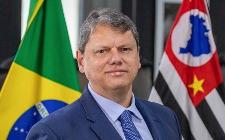 Tarcísio de Freitas, de terno azul, entre as bandeiras do Brasil e do estado de São Paulo
